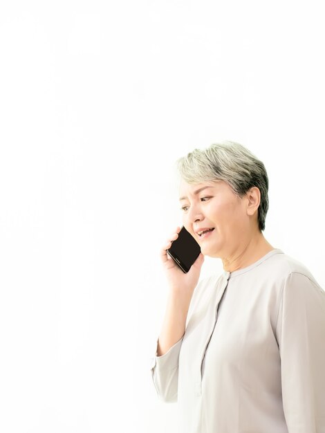 Mujer asiática mayor hablando por su teléfono móvil en fondo blanco.