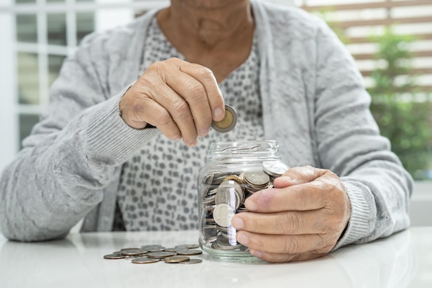 Mujer asiática mayor o anciana sosteniendo contando dinero de monedas en un frasco de vidrio Problema de ahorro de pobreza en la jubilación