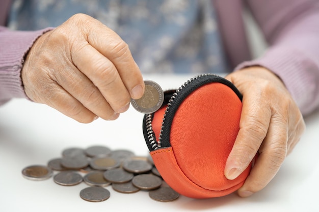 Mujer asiática mayor o anciana sosteniendo contando monedas en el bolso Problema de ahorro de pobreza en la jubilación