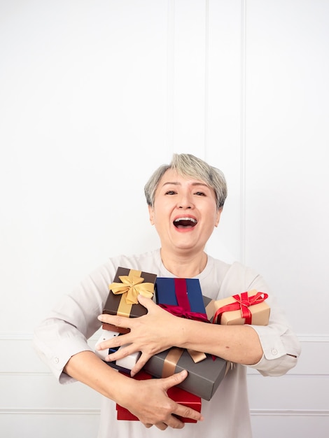 Mujer asiática mayor que sostiene el montaje de cajas de regalo, disfrutando de muchos mejores regalos.