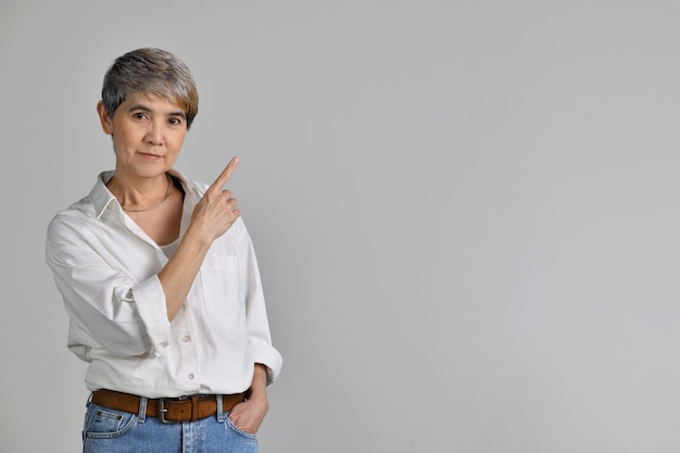 Mujer asiática de mediana edad apuntando con el dedo hacia arriba en el espacio vacío de la copia de texto aislado sobre fondo blanco. mirando a la camara