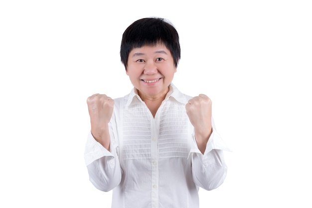 Mujer asiática de mediana edad en camisa blanca levantando sus puños expresando éxito en algo aislado sobre fondo blanco.