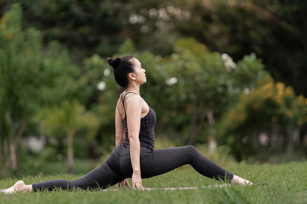 Una mujer asiática de mediana edad segura de sí misma en traje deportivo haciendo ejercicio de yoga en la estera de yoga al aire libre en el patio trasero por la mañana. Mujer joven haciendo ejercicio de yoga al aire libre en el parque público de la naturaleza