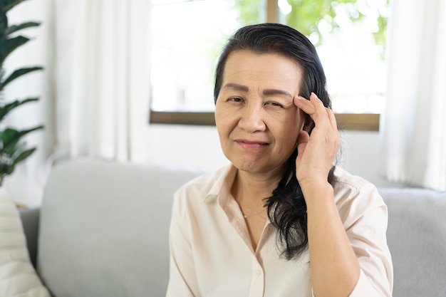 Mujer asiática de mediana edad tocando la frente con dolor de cabeza que sufre de migraña xA sintiéndose enferma o deprimida