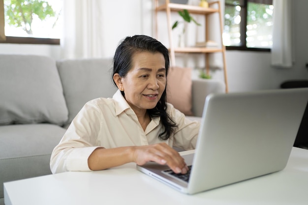 Mujer asiática de mediana edad Trabaja desde casa mujer anciana sonriente hermosa mujer asiática madura en portátil con concepto de tecnología