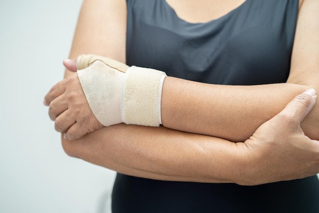 La mujer asiática de mediana edad usa un vendaje elástico para tratar el síndrome de De Quervain en la mano y el dedo en la oficina.