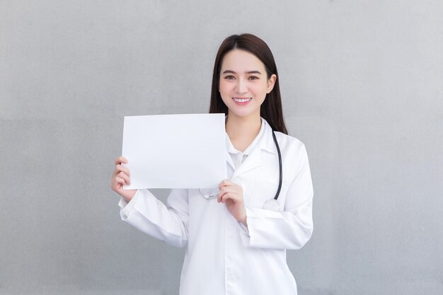 Mujer asiática médico profesional que usa bata médica sostiene y muestra papel blanco para presentar algo en concepto de atención médica.