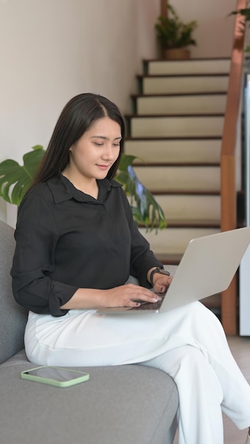 Mujer asiática milenaria descansando en el sofá y usando una computadora portátil