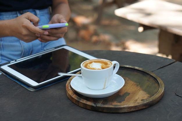 Mujer asiática mirando ganancias en su teléfono en una cafetería donde puede ir a trabajar en medio de la naturaleza verde