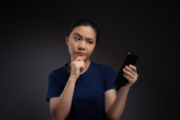 Mujer asiática mirando noticias de lectura de teléfonos inteligentes y se siente confundida.