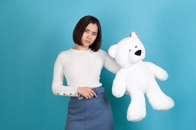 Mujer asiática molesta, ofendida y triste en ropa casual sosteniendo un gran oso de peluche blanco por la oreja