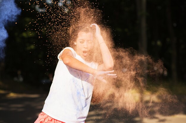 Mujer asiática morena emocional jugando con pintura seca naranja y azul en el festival de colores Holi