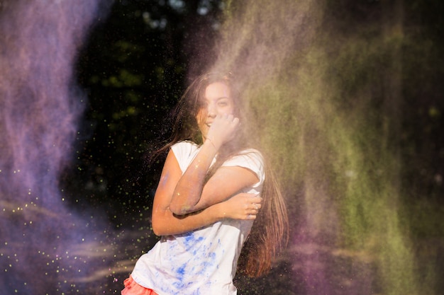 Mujer asiática morena emocional con el pelo largo posando en una nube de pintura Holi