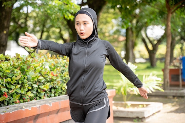 Mujer asiática musulmana estirando su brazo durante el ejercicio al aire libre