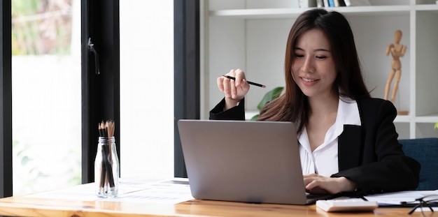 Mujer asiática de negocios con ordenador portátil para hacer matemáticas finanzas en un escritorio de madera en la oficina, impuestos, contabilidad, concepto financiero