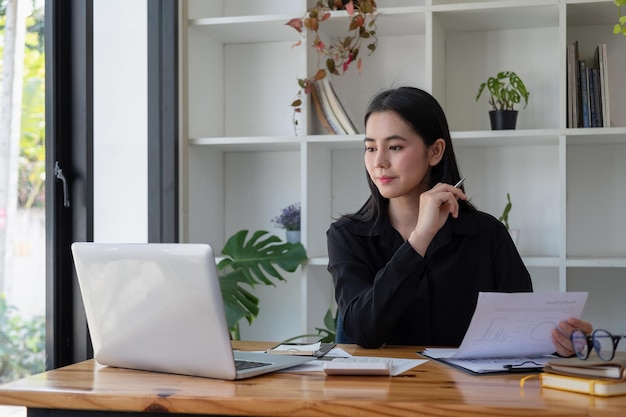 Mujer asiática de negocios que usa un teléfono inteligente para hacer finanzas matemáticas en un escritorio de madera en la oficina, impuestos, contabilidad, concepto financiero.