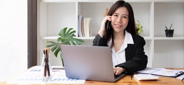 Mujer asiática de negocios con smartphone para hacer finanzas matemáticas en un escritorio de madera en la oficina, impuestos, contabilidad, concepto financiero