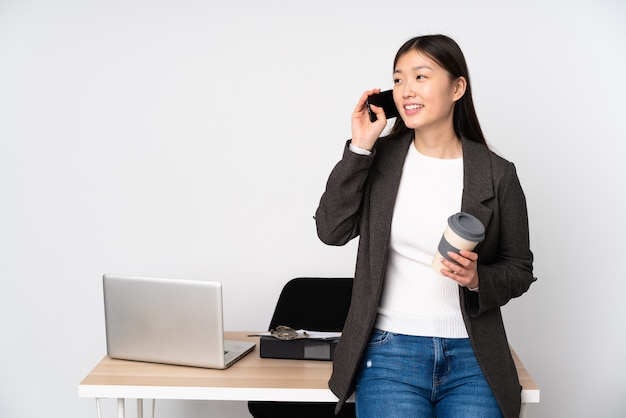 Mujer asiática de negocios en su lugar de trabajo aislado en blanco con café para llevar y un móvil