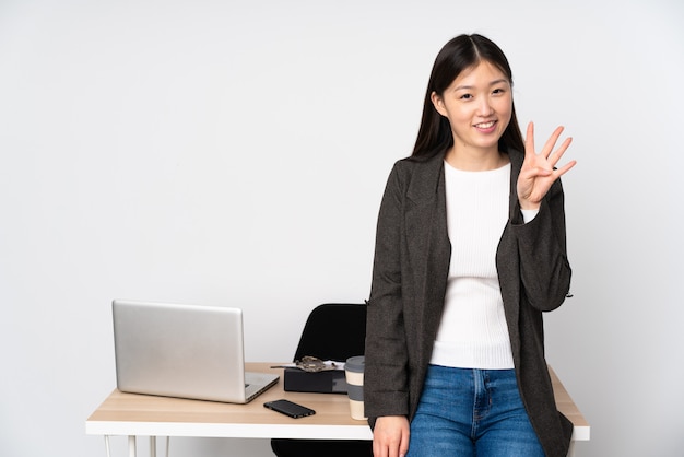 Mujer asiática de negocios en su lugar de trabajo aislado en el espacio en blanco feliz y contando cuatro con los dedos