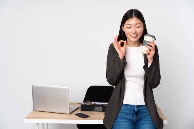 Mujer asiática de negocios en su lugar de trabajo en la pared blanca en pose zen