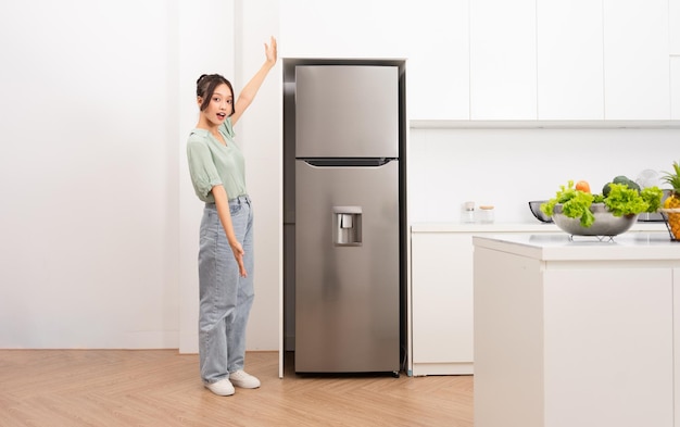 Foto mujer asiática parada al lado del refrigerador en la cocina