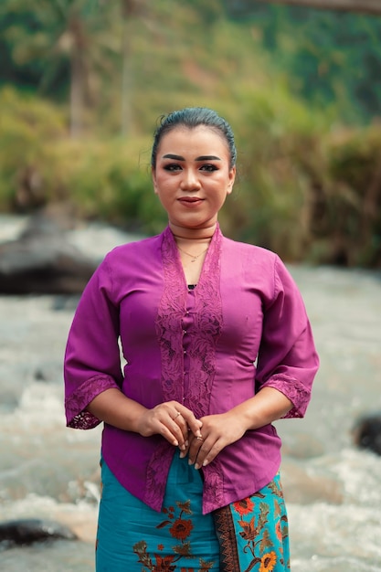 Mujer asiática parada frente al río mientras usa un vestido morado con hermoso maquillaje y río en el fondo