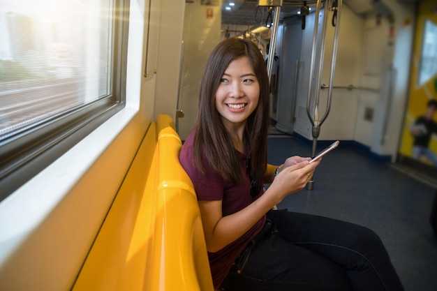 Mujer asiática pasajera con traje casual usando el teléfono móvil inteligente en el Skytrain