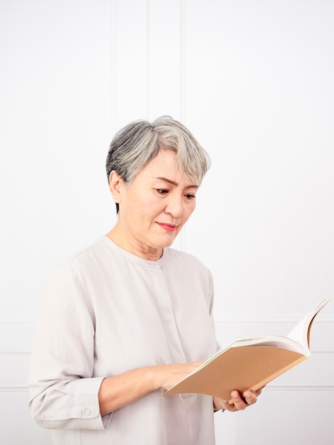 Mujer asiática de pelo gris Senior sosteniendo y leyendo el libro en casa.