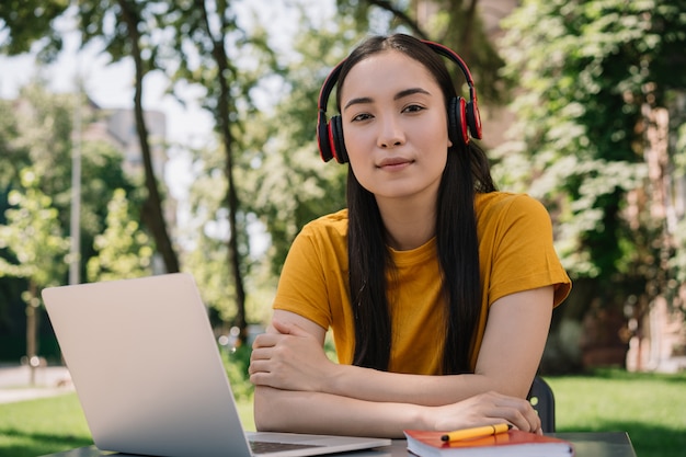 Mujer asiática pensativa usando audífonos, mirando a la cámara