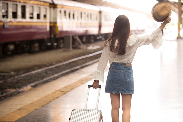 Mujer asiática de pie llevando equipaje en la plataforma de la estación de tren