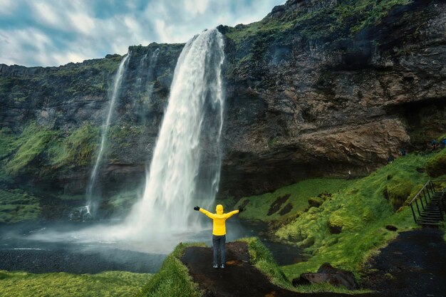 Mujer asiática de pie y mirando la cascada Moody Seljalandsfoss que fluye desde el acantilado en verano en Islandia