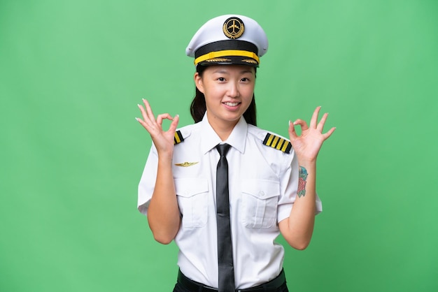Mujer asiática piloto de avión sobre un fondo aislado que muestra un signo de ok con los dedos