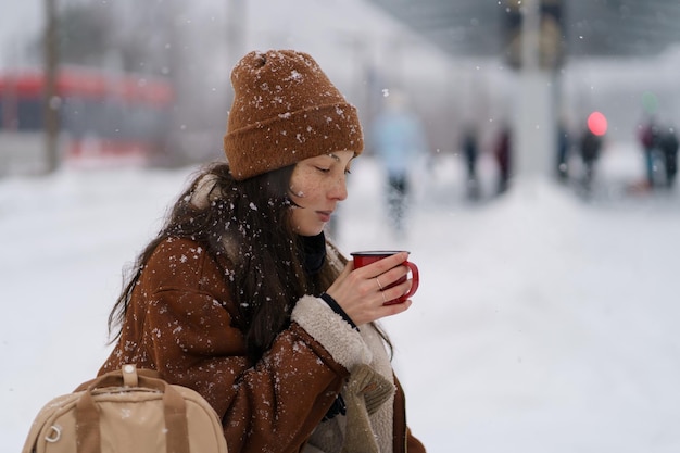 Mujer asiática en la plataforma ferroviaria tratando de mantenerse caliente mientras espera el tren retrasado por las nevadas