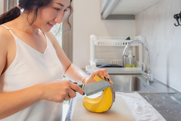 Mujer asiática positiva ama de casa cocinando comida vegetariana saludable en la cocina de casa Mujer feliz haciendo tareas domésticas Mujer asiática cortando verduras en la mesa de la cocina