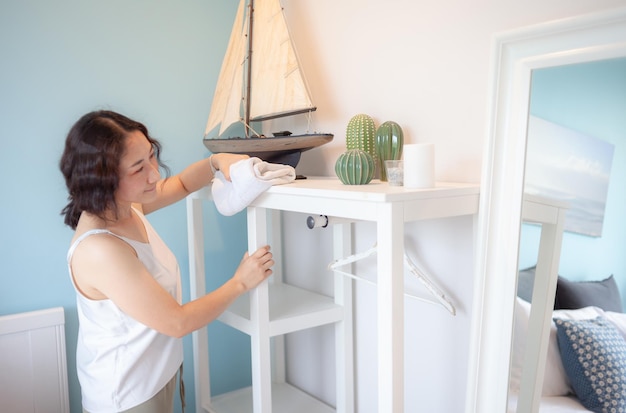 Mujer asiática positiva ama de casa limpiando casa moderna Mujer feliz haciendo tareas domésticas Ama de casa asiática Limpiando estante muebles cama espejo sofá y electrodomésticos