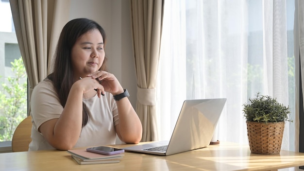 Mujer asiática positiva usando computadora portátil navegando por internet comprando en línea en casa