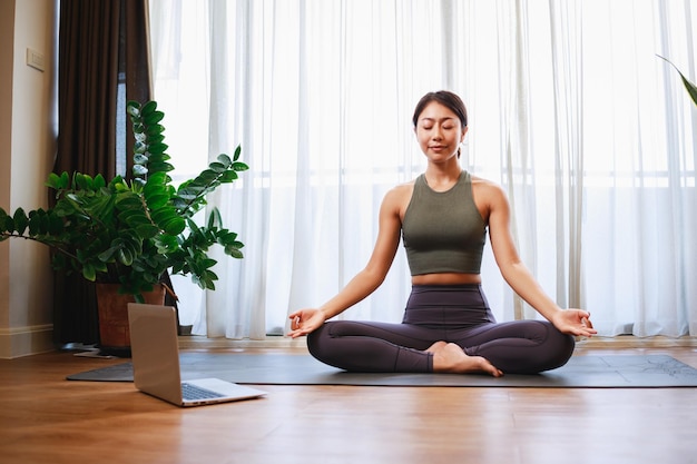 Mujer asiática practicando yoga del curso en línea de yoga en una videoconferencia en una computadora portátil en casa
