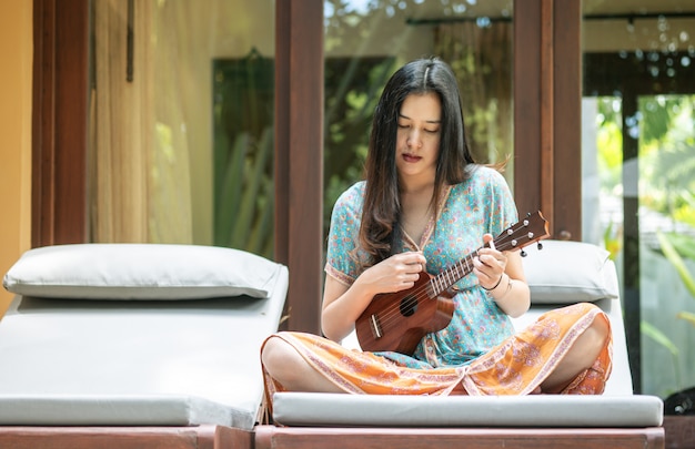 Mujer asiática del primer que toca el ukelele en el sofá en la terraza