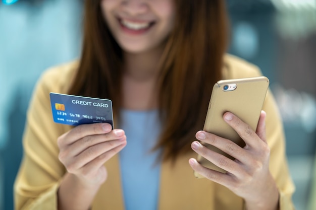 Mujer asiática del primer que usa la tarjeta de crédito con el móvil para las compras en línea en grandes almacenes