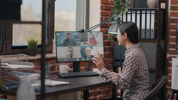 Mujer asiática que asiste a una reunión de negocios en una videollamada, conversando sobre proyectos y estrategias. Empleado hablando con compañeros de trabajo en videoconferencia remota en computadora. Disparo de mano