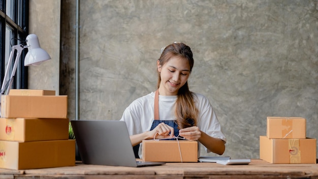 Una mujer asiática que ata un paquete a la caja de un cliente, es propietaria de una tienda en línea, empaca y envía a través de una empresa de transporte privada Conceptos de venta y compras en línea