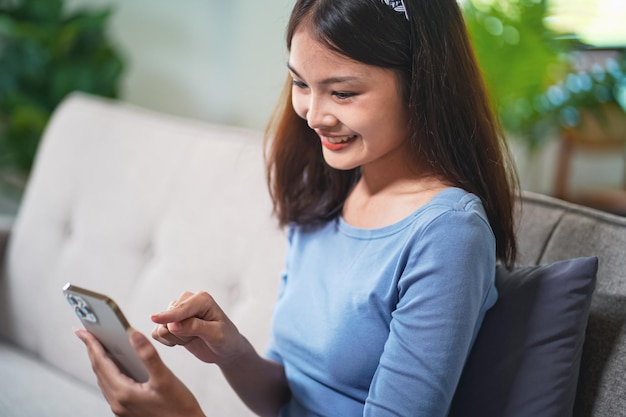 Mujer asiática que controla el teléfono móvil doméstico inteligente con la aplicación inteligente para el hogar en la pantalla táctil de la sala de estar tecnología ai Sistema de control remoto del hogar