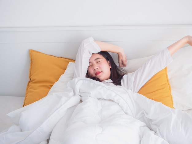 Mujer asiática que estira en la cama después de despertar