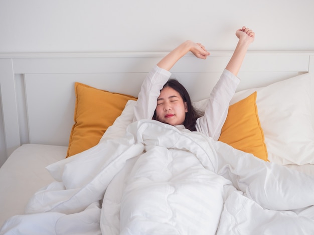 Mujer asiática que estira en la cama después de despertar