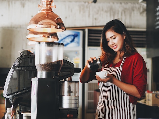 Mujer asiática que hace una taza de taza de café en el café