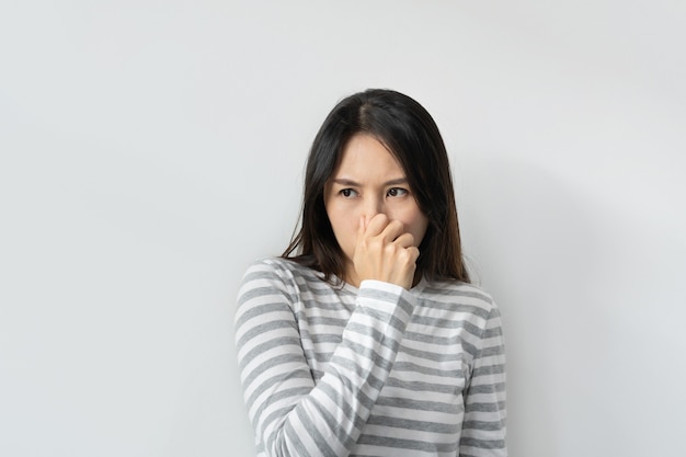 Mujer asiática que huele algo apestoso y repugnante, un olor intolerable, conteniendo la respiración con los dedos en la nariz. Chica aprieta la nariz con los dedos mira con disgusto algo huele mal. Copia espacio