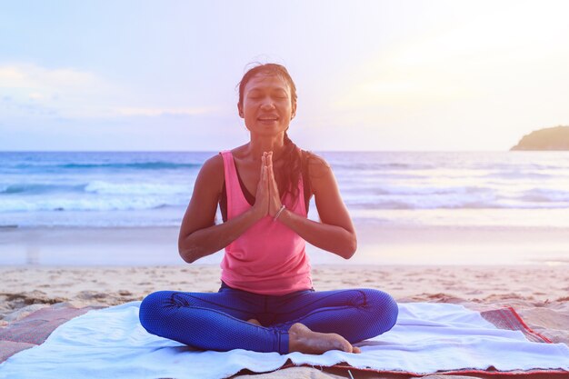Mujer asiática que juega yoga y ejercicio en la playa tropical en Tailandia