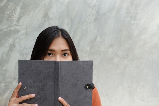 Mujer asiática que lee un libro en un fondo gris.