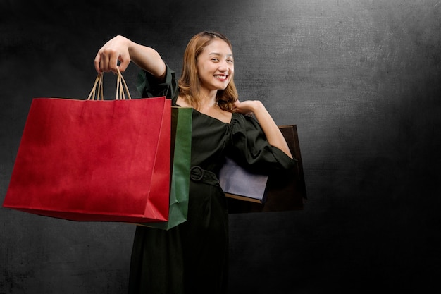 Mujer asiática que lleva una bolsa de compras con un fondo de pared negra. Concepto de viernes negro