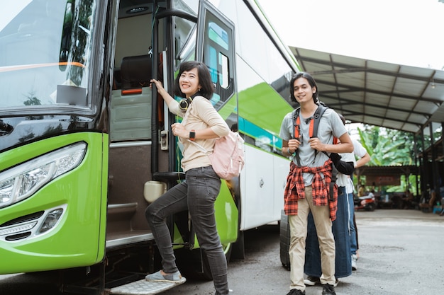 Mujer asiática que lleva una mochila y auriculares mientras sostiene la manija de la puerta se sube al autobús con la pared de pasajeros haciendo fila para subir al autobús